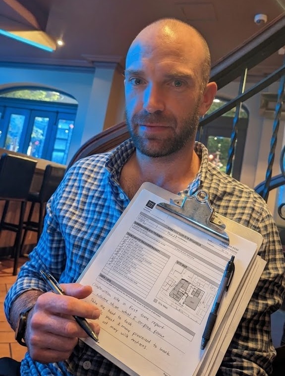 Field manager holding a clipboard with a printed site report form, checklist, site map and handwritten notes from the day's work