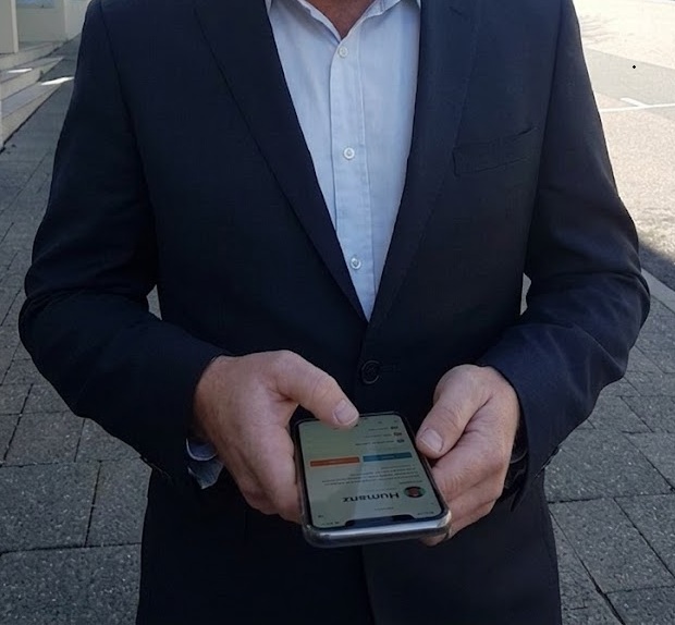 Manager in a suit checking the Humanz workforce app on a phone outside, the office end of the platform the field crew uses